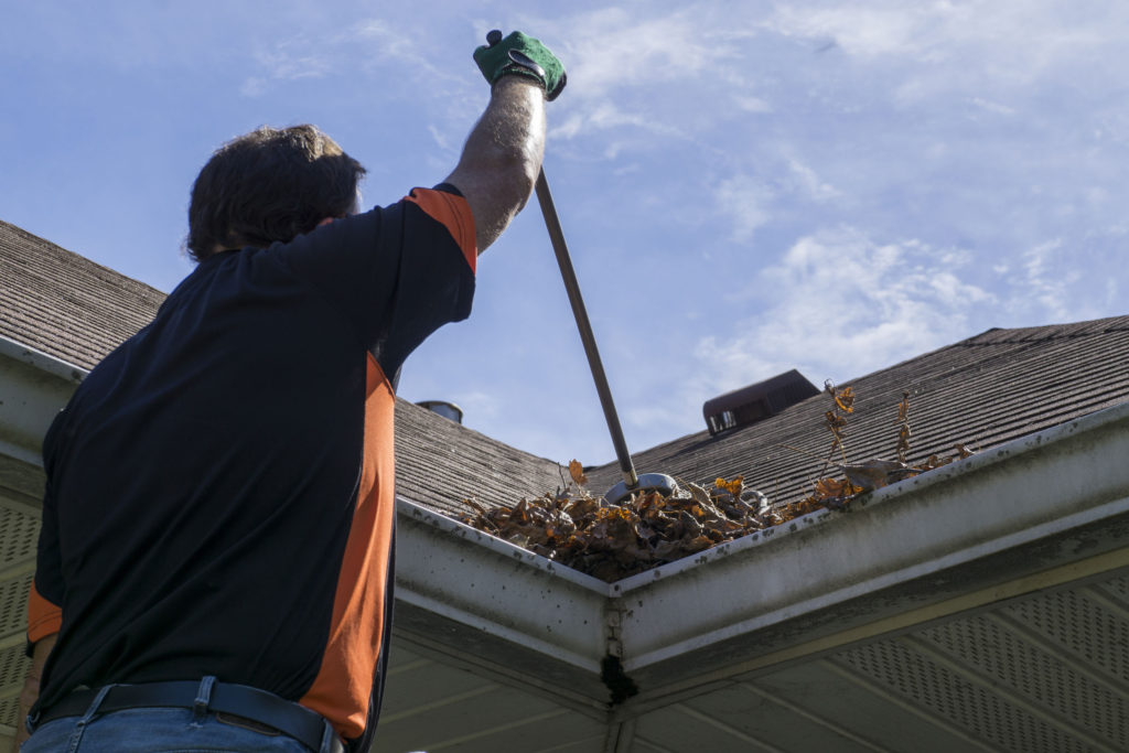 Worker sweeping leaves from roof spring maintenance